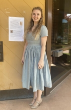 Flannery Jamison standing outside in front of a conference poster wearing a light green dress and heels. 
